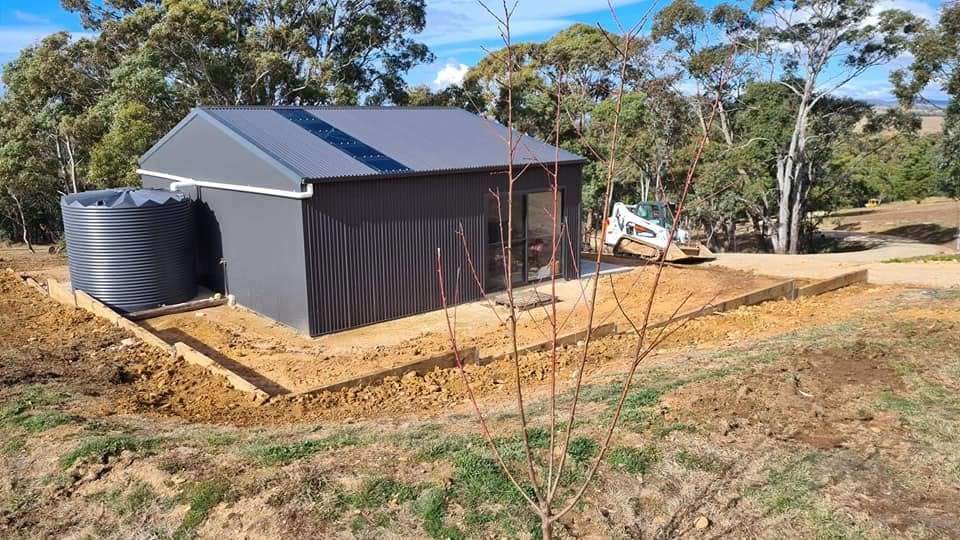Bobcat excavator working beside a newly built rural shed and water tank